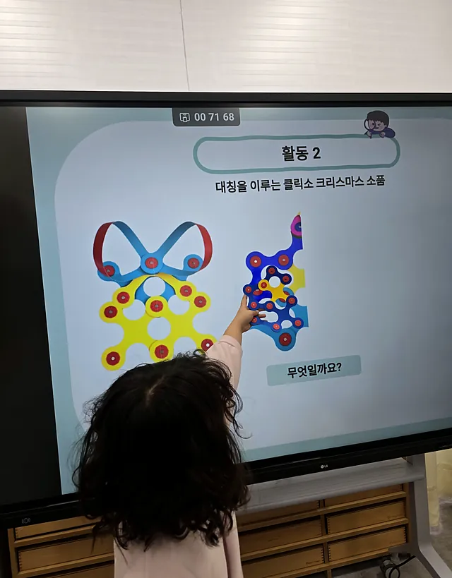 전자칠판에서 대칭 모양을 찾아 가리키는 아이의 뒷모습
