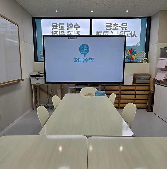 처음수학 로고가 뜬 큰 화면 앞에 모둠 책상이 놓인 사고력 랩
